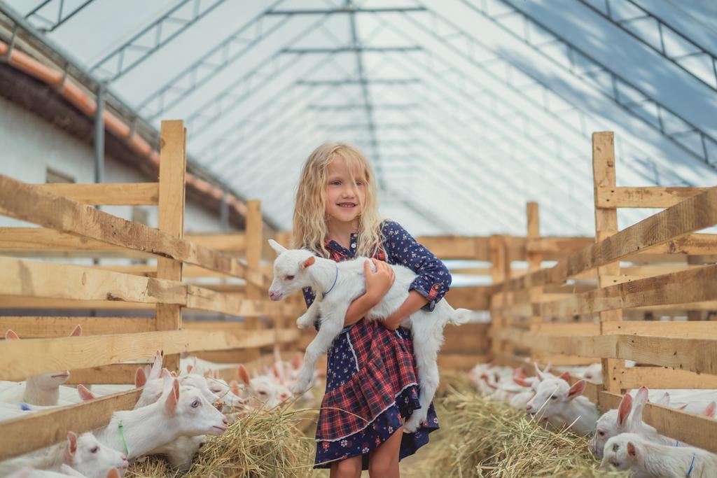 smiling adorable kid holding goat at farm - Photo, Image
