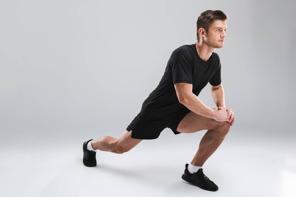 Retrato de um jovem desportista confiante fazendo exercícios de alongamento isolados sobre fundo cinza
 - Foto, Imagem