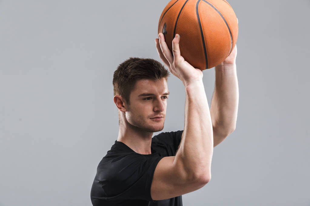 Πορτρέτο του ένα συμπυκνωμένο νεαρό αθλητή παίζοντας μπάσκετ που απομονώνονται σε γκρίζο φόντο - Φωτογραφία, εικόνα