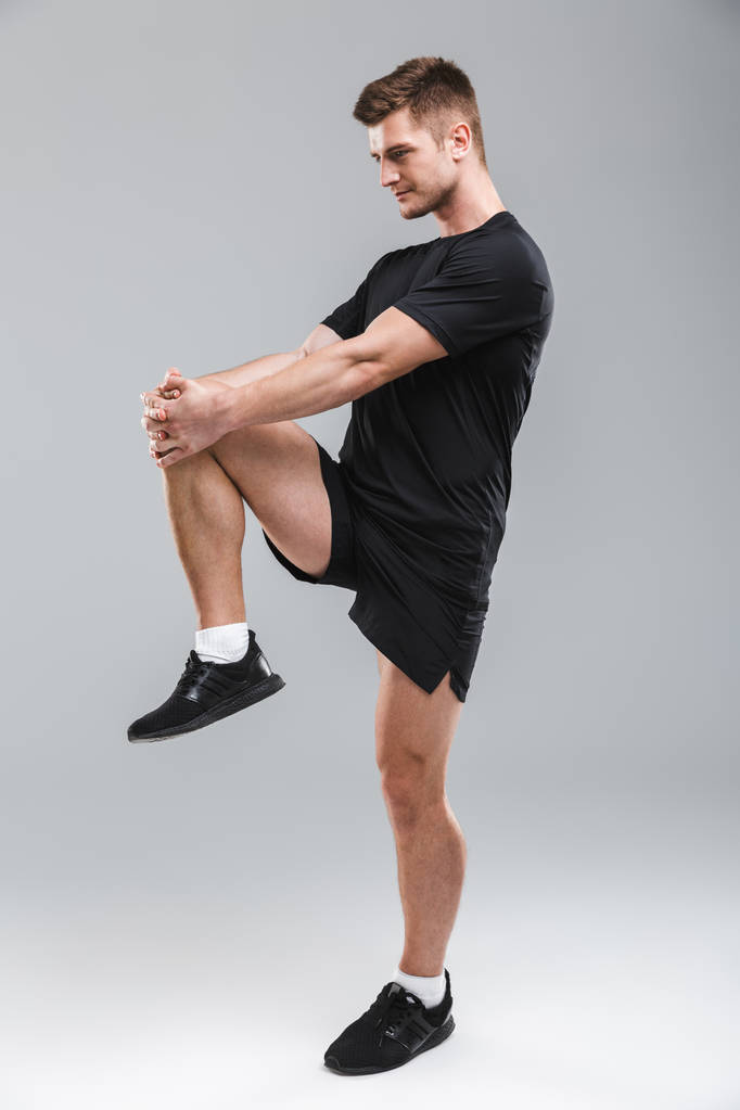 Retrato de un joven deportista enfocado haciendo ejercicios de estiramiento aislados sobre fondo gris
 - Foto, imagen