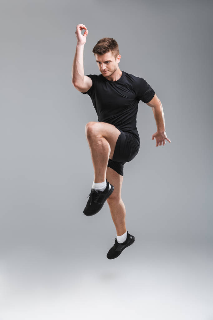 Retrato de comprimento total de um jovem desportista forte pulando isolado sobre fundo cinza
 - Foto, Imagem