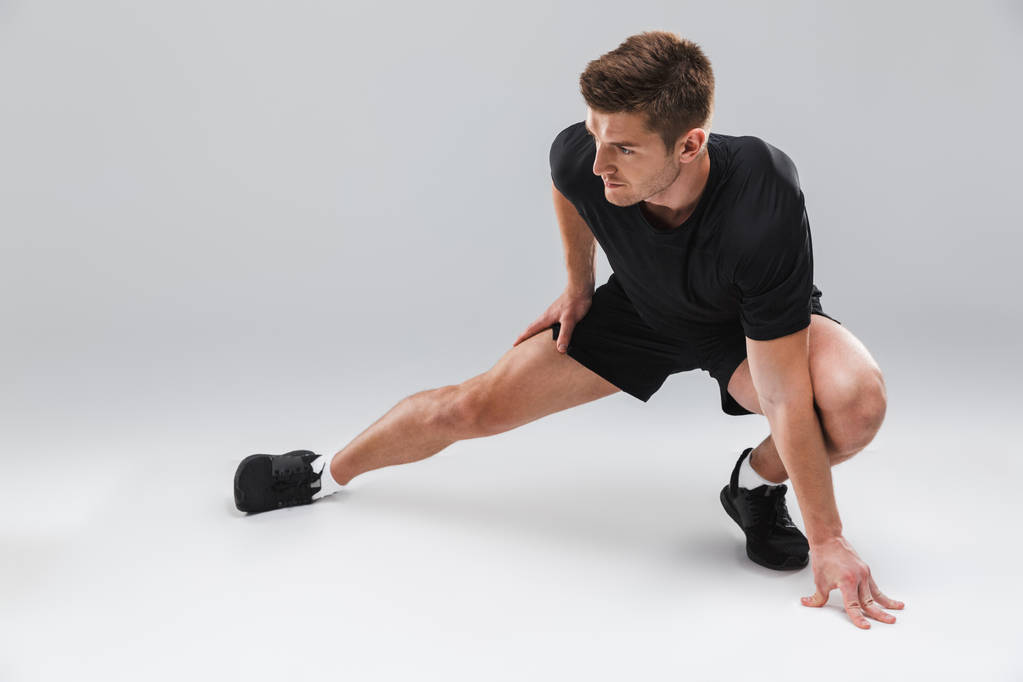 Retrato de un joven deportista motivado haciendo ejercicios de estiramiento aislados sobre fondo gris
 - Foto, imagen
