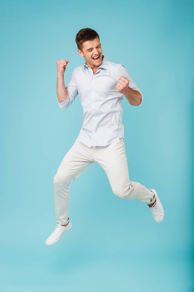 Afbeelding van emotionele Kaukasische jongeman geïsoleerde springen over blauwe achtergrond winnaar gebaar maken. - Foto, afbeelding