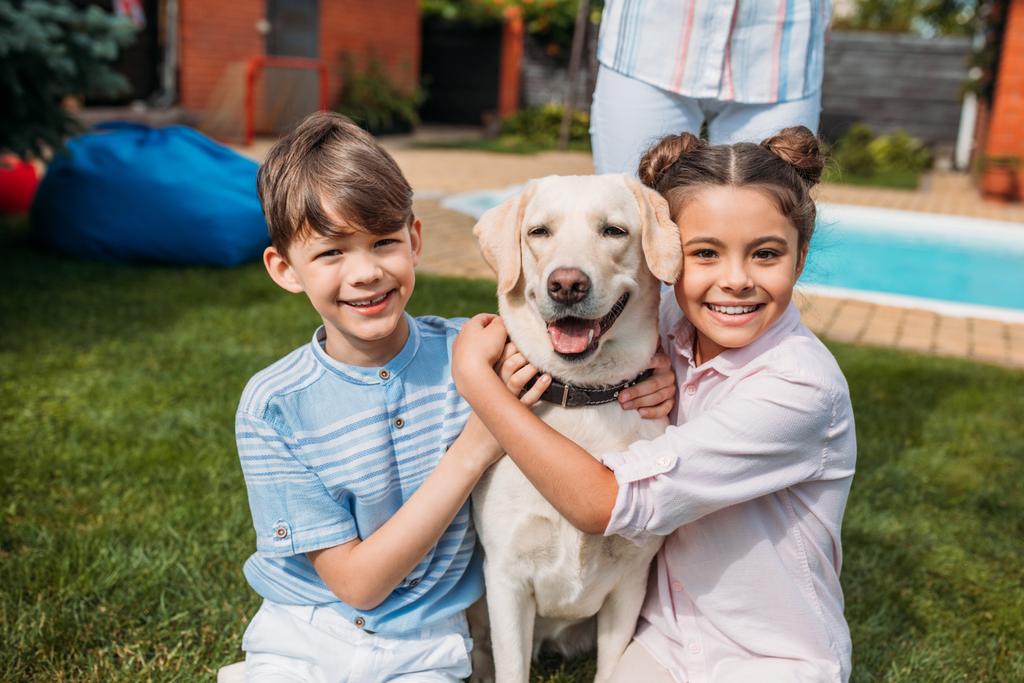 Lächelnde Kinder umarmen Labrador-Hund auf Hinterhof - Foto, Bild