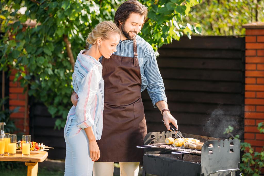 coppia sorridente avendo barbecue in cortile il giorno d'estate
 - Foto, immagini