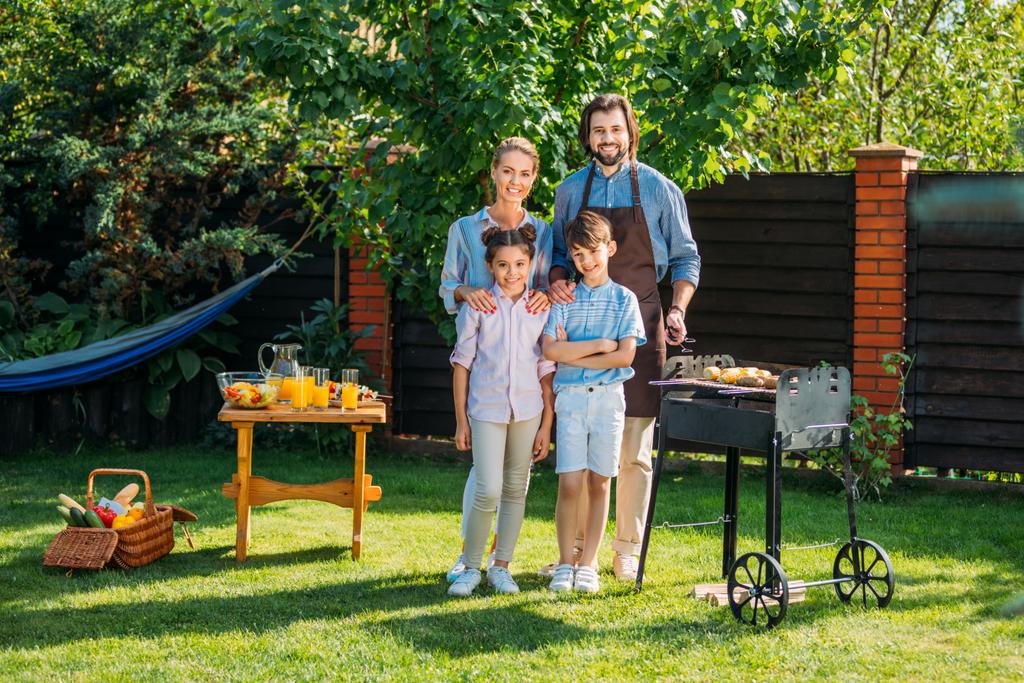 gelukkige familie camera kijken terwijl het hebben van barbecue samen op achtertuin op zomerdag - Foto, afbeelding