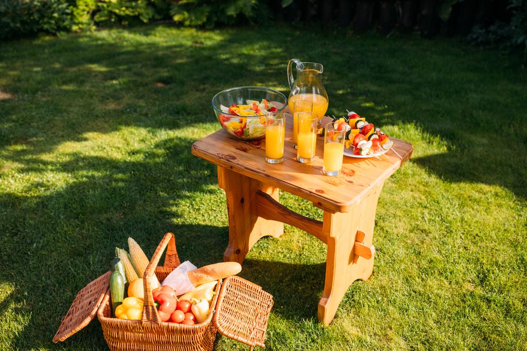 zár megjelöl kilátás kosár élelmiszer-piknik, pohár gyümölcslé, friss salátával, fából készült szék a zöld gyep - Fotó, kép
