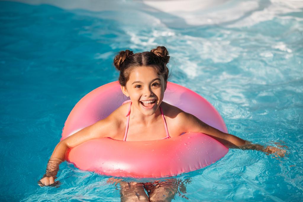 portrait of happy kid with inflatable ring swimming in swimming pool on summer day - Photo, Image