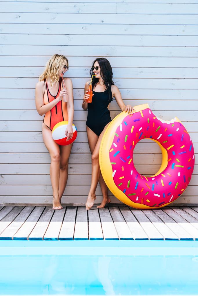 hermosas mujeres jóvenes sonrientes con artículos de playa que beben bebidas de verano en la piscina
   - Foto, Imagen