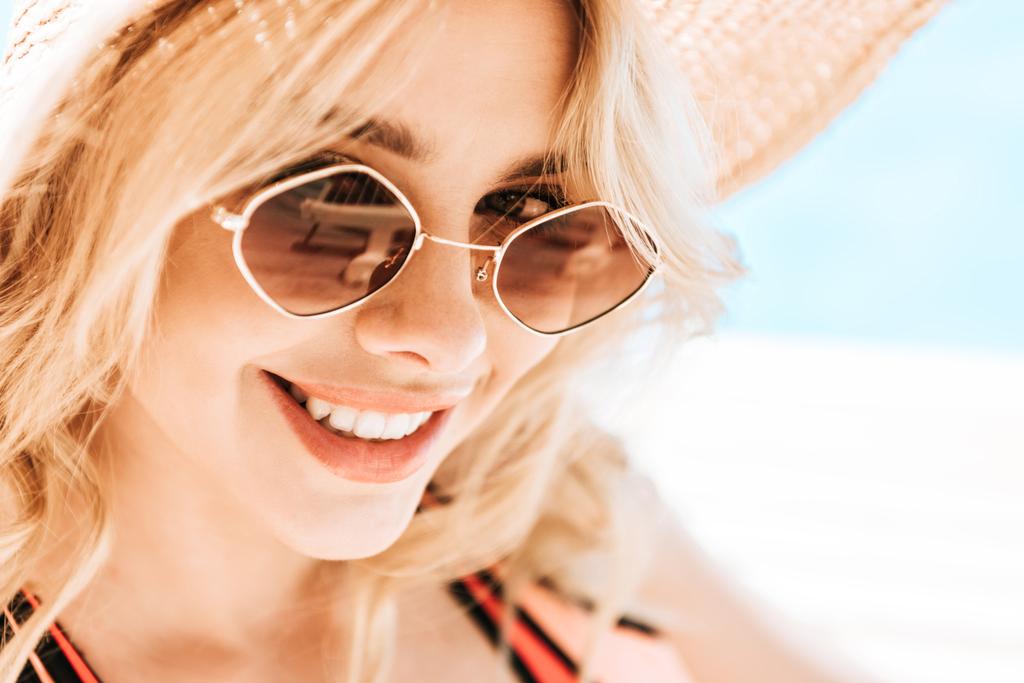 портрет красивой молодой блондинки в солнцезащитных очках и плетеной шляпе, улыбающейся в камеру у бассейна
 - Фото, изображение