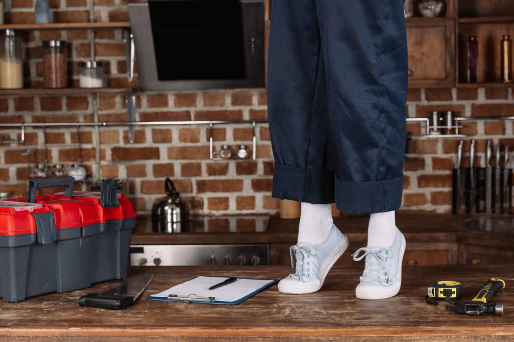 repairwoman iş pantolon ve Beyaz Ayakkabı ayak mutfak masasının üzerinde duran kırpılmış atış - Fotoğraf, Görsel