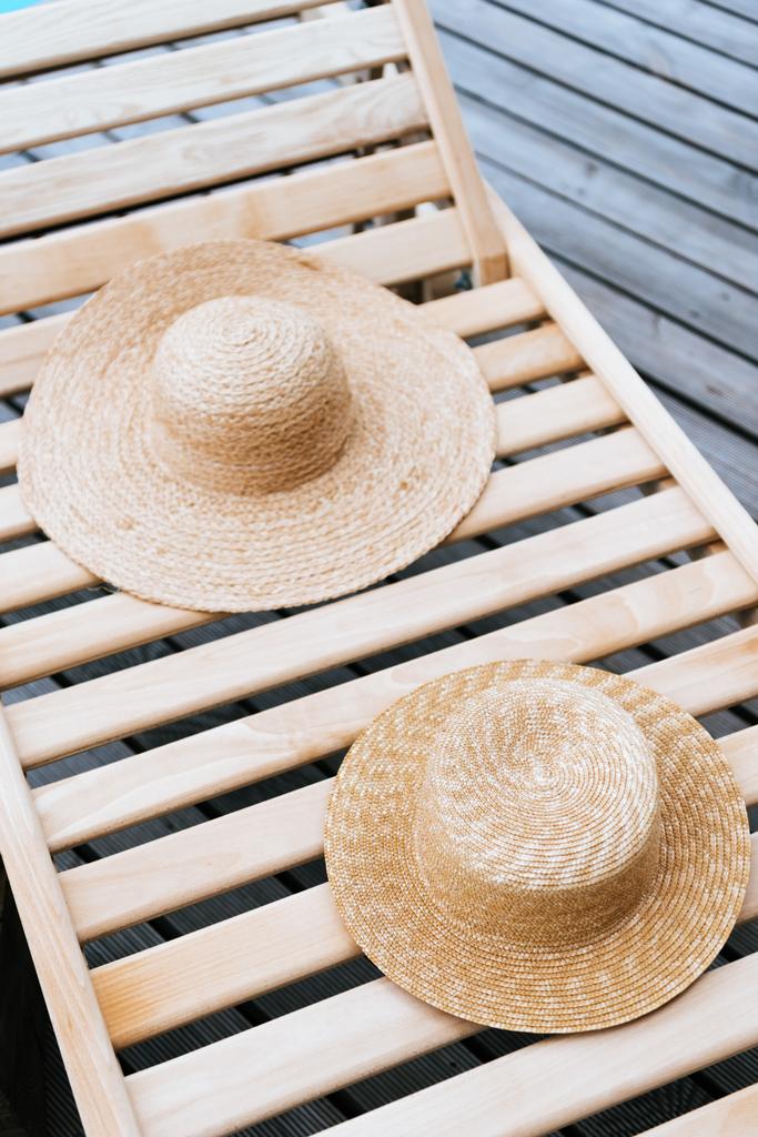 twee stijlvolle rieten hoeden op chaise lounge bij zwembad - Foto, afbeelding