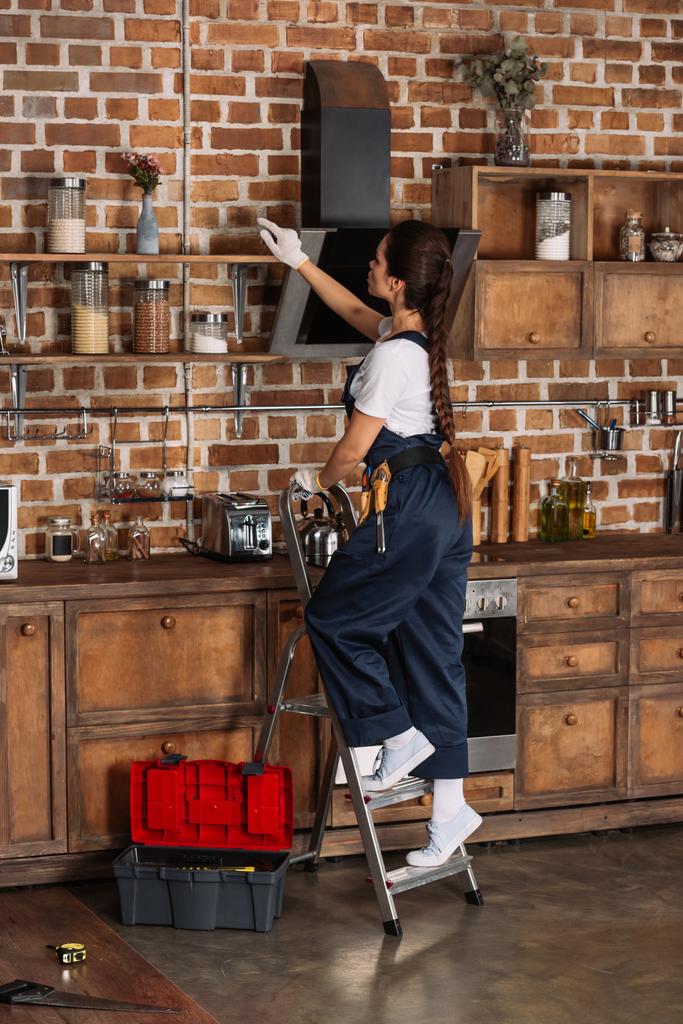 beautiful young repairwoman standing on stepladder at kitchen - Photo, Image