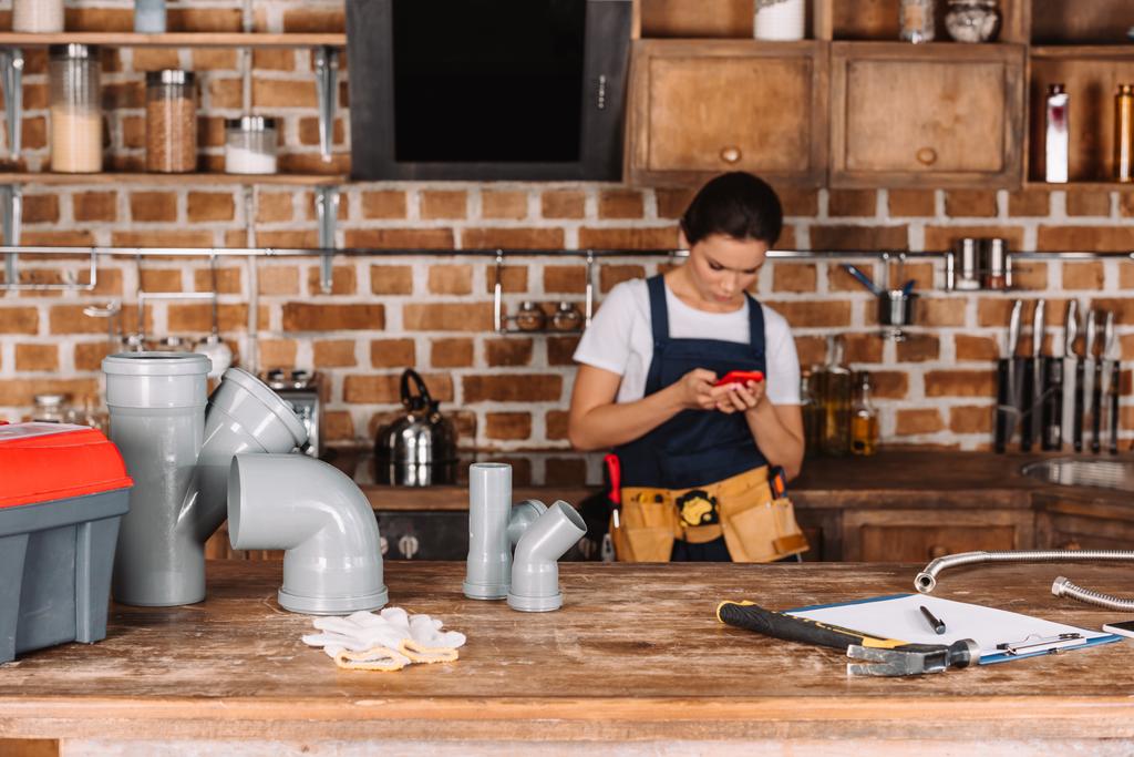 schöne junge Klempnerin mit Smartphone in der Küche - Foto, Bild