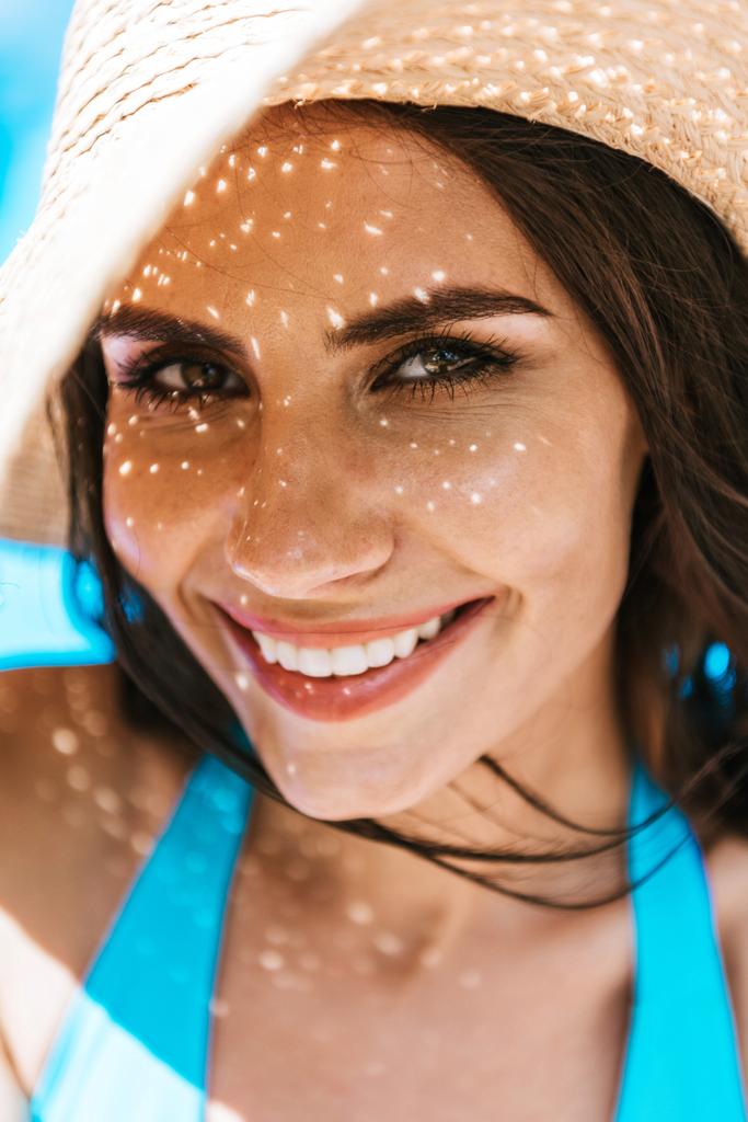 portrét krásné brunetka žena v slamák se usmívá na kameru na bazénu - Fotografie, Obrázek