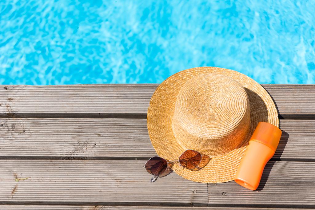 vista superior do chapéu de vime, óculos de sol e protetor solar perto da piscina
   - Foto, Imagem