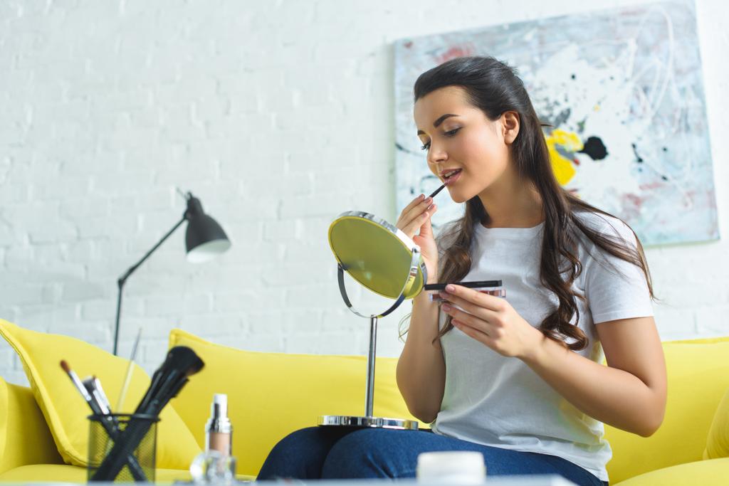 mladá žena nanesení rtěnky a přitom make-up na gauči doma - Fotografie, Obrázek