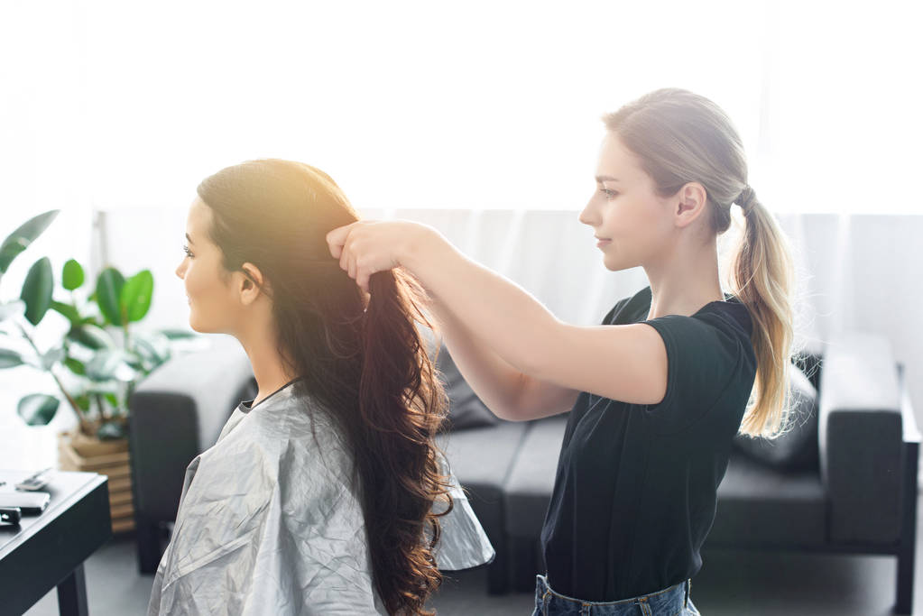 side view of hairstylist doing hairstyle to young woman on chair - Photo, Image