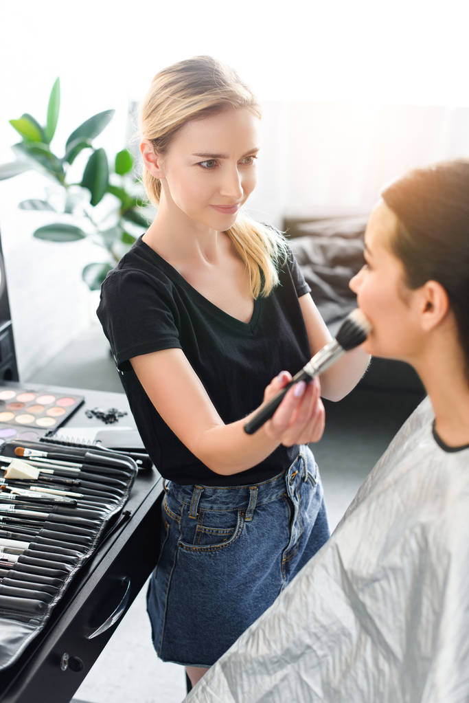 enfoque selectivo de artista de maquillaje aplicando polvo en la cara de las mujeres con cepillo
 - Foto, imagen
