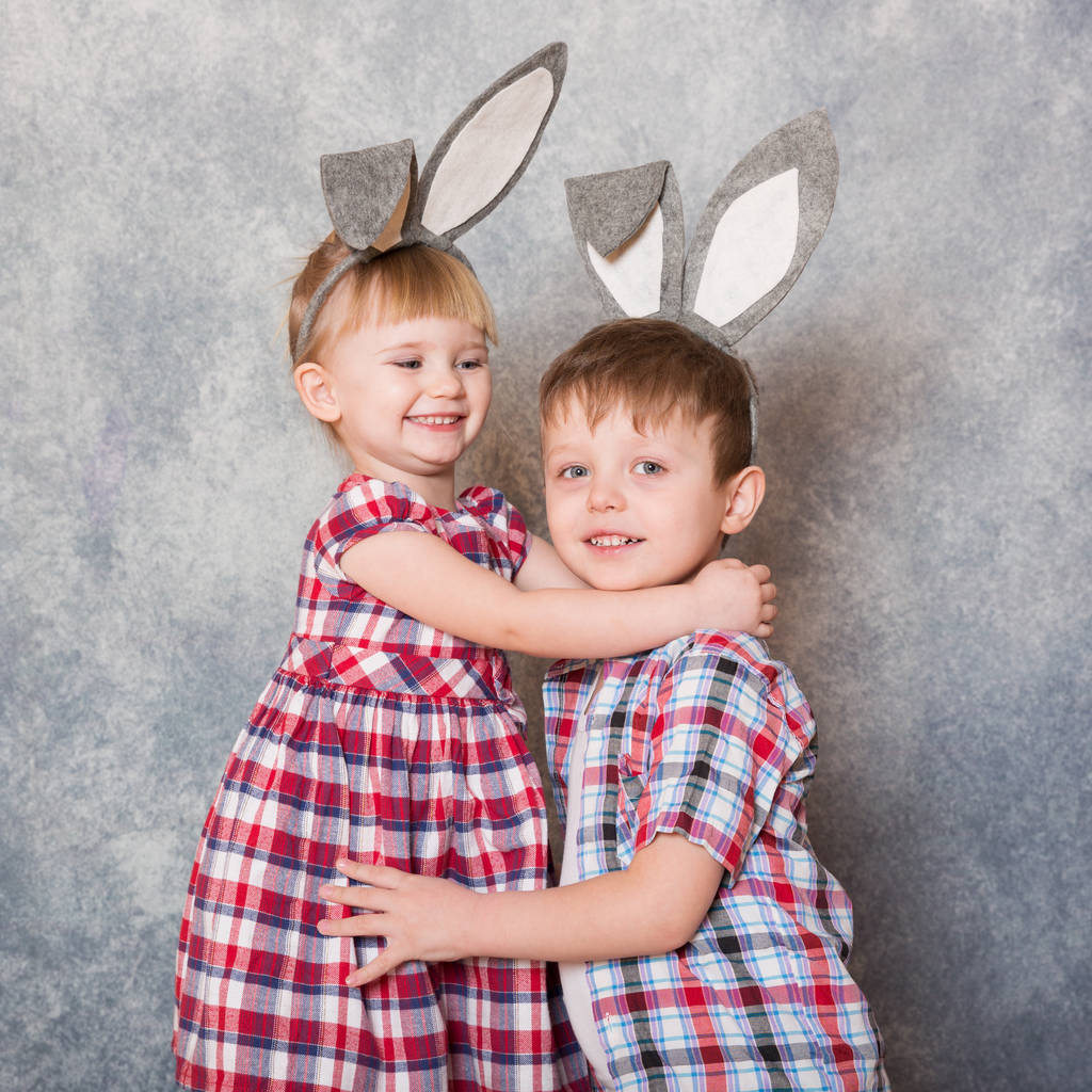 Dos niños, una niña y un niño con orejas de conejo de Pascua en la cabeza se ríen y juegan. Semana Santa familiar. Copiar espacio
. - Foto, Imagen
