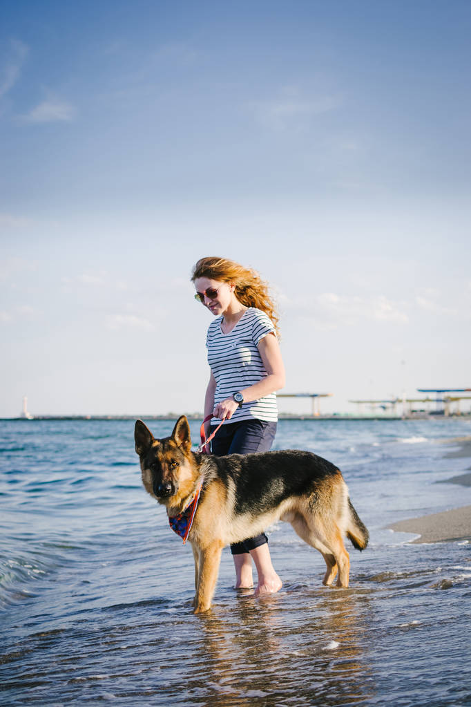 Feliz joven mujer caminando con su perro pastor alemán al aire libre en la playa
 - Foto, imagen