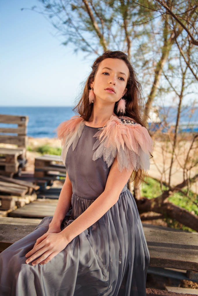 portrait of a longing dreaming young girl in a gray dress with feathers and pink earrings looking out into the distance - Photo, Image