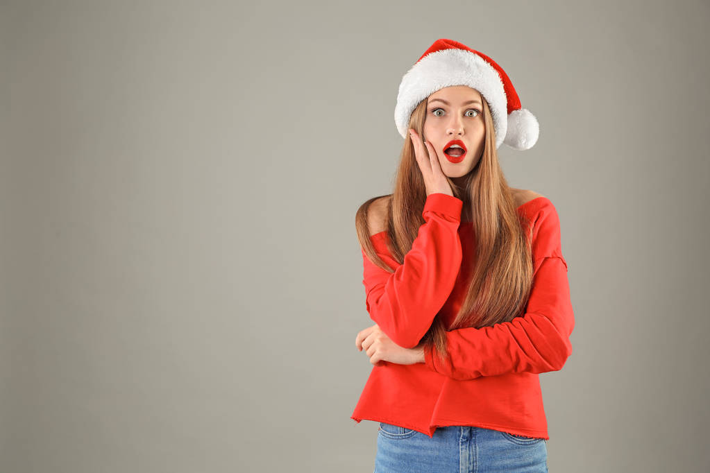 Young beautiful woman in Santa hat on grey background. Christmas celebration - Photo, Image