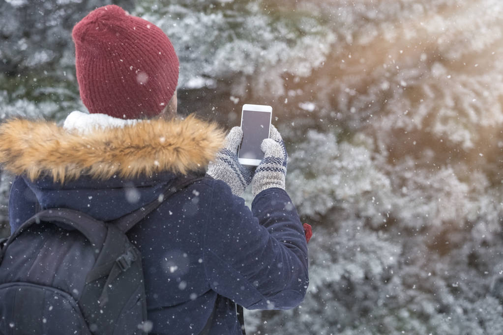 Vue arrière du jeune homme utilisant un smartphone le jour neigeux
. - Photo, image