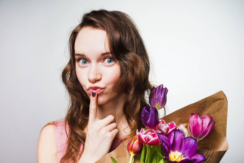 hauska kaunis sinisilmäinen tyttö poseeraa suuri kukkakimppu, laita sormi huulilleen
 - Valokuva, kuva