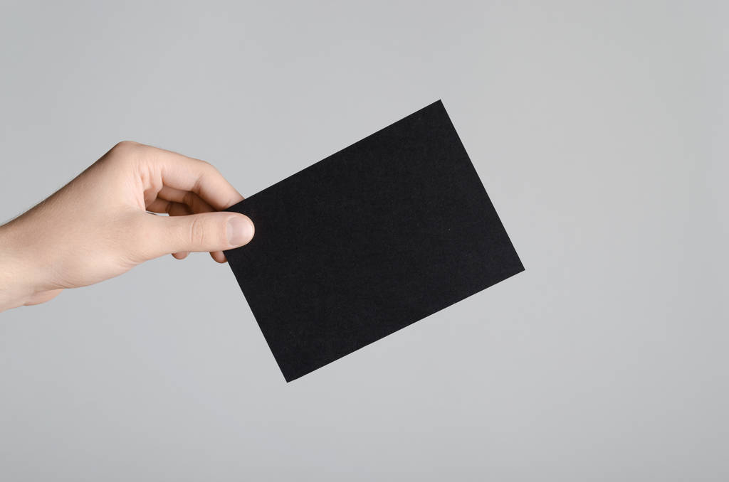 Black A6 Flyer / Postcard / Convite Mock-Up - Mãos masculinas segurando um folheto preto em um fundo cinza. - Foto, Imagem
