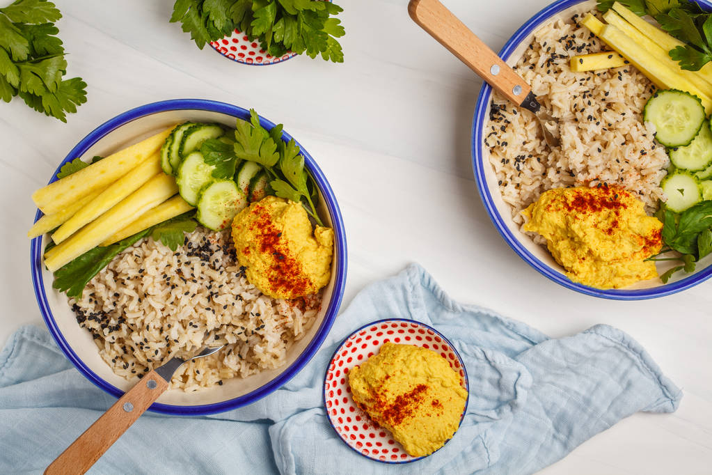 Vegan lunch met rijst, hummus en groenten in witte platen, bovenaanzicht. Gezond vegetarisch voedsel concept. - Foto, afbeelding