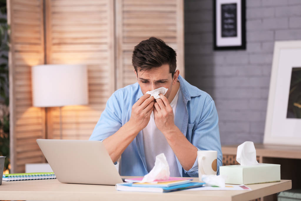 Sad exhausted man with tissue suffering from cold while working with laptop at table - Photo, Image