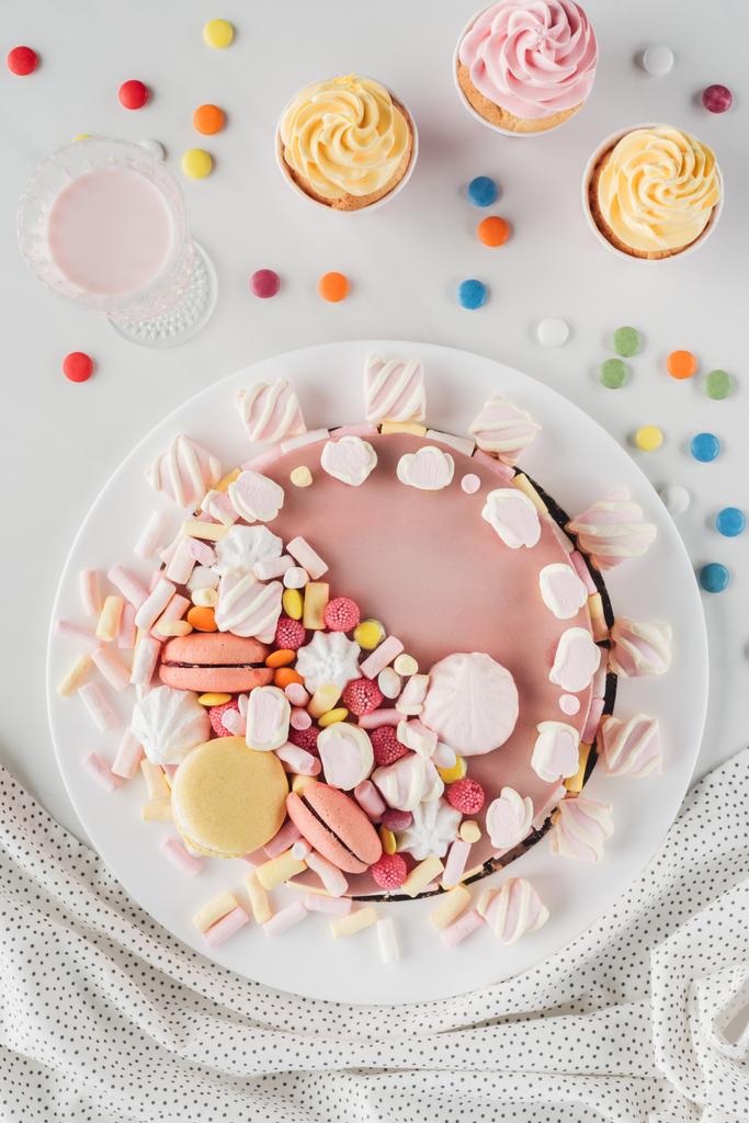 bovenaanzicht van de cake van de kindverjaardag met marshmallows, snoepjes en zoete cupcakes op tafel  - Foto, afbeelding