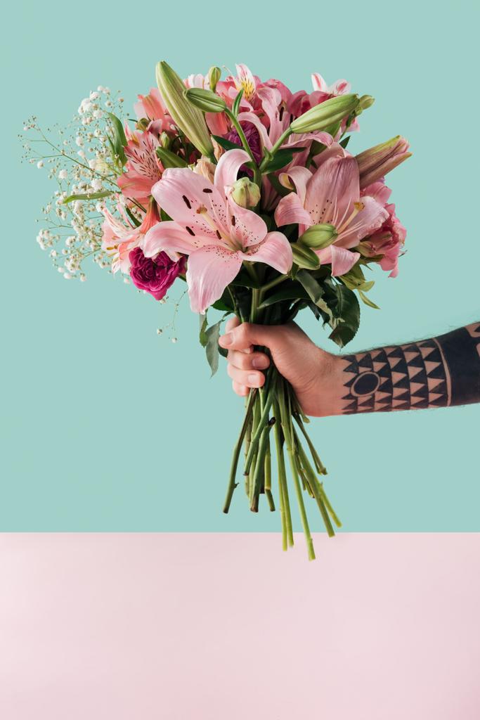 abgeschnittene Ansicht tätowierter männlicher Hand mit einem Strauß rosa Lilienblüten - Foto, Bild