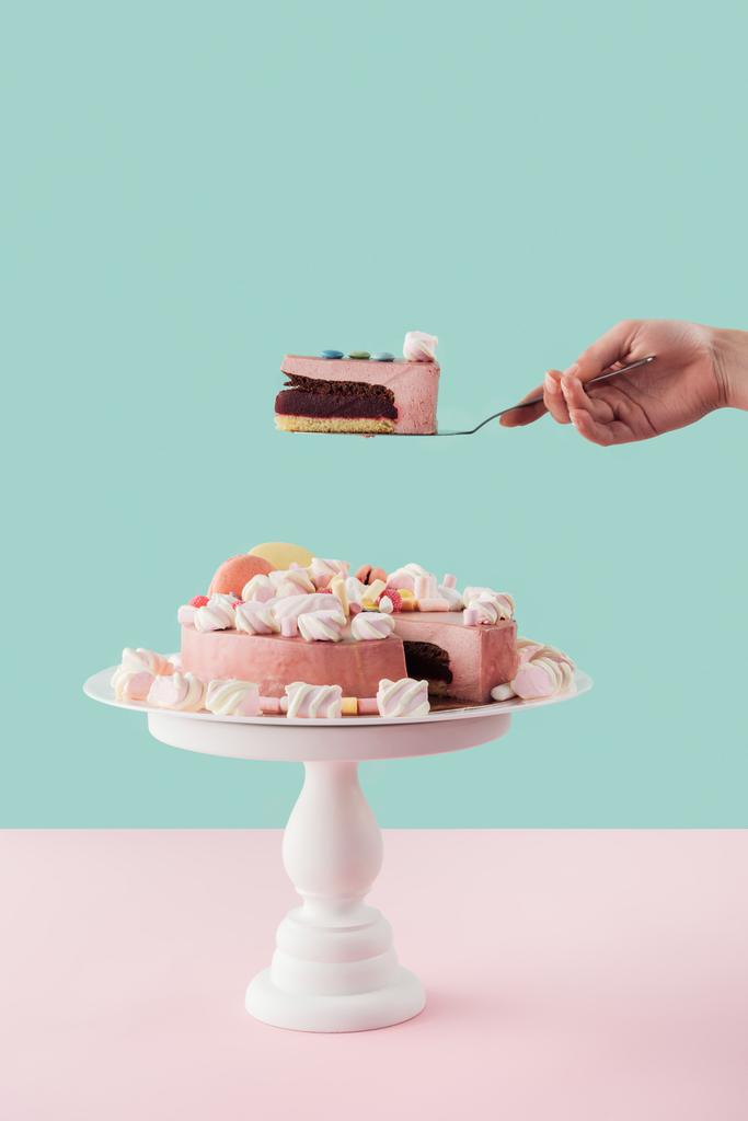 abgeschnittene Ansicht einer Frau mit einem Stück Kuchen auf einer Schaufel über einem großen Kuchen auf einem Ständer - Foto, Bild
