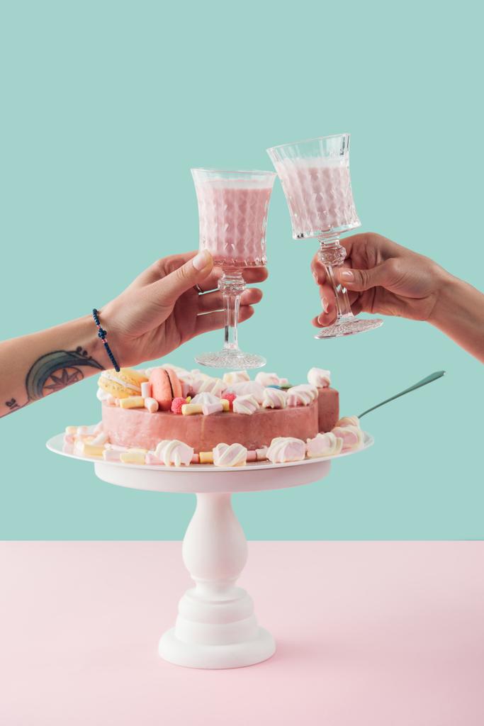 cropped view of people clinking with glasses of milkshake over cake with marshmallows on stand - Photo, Image