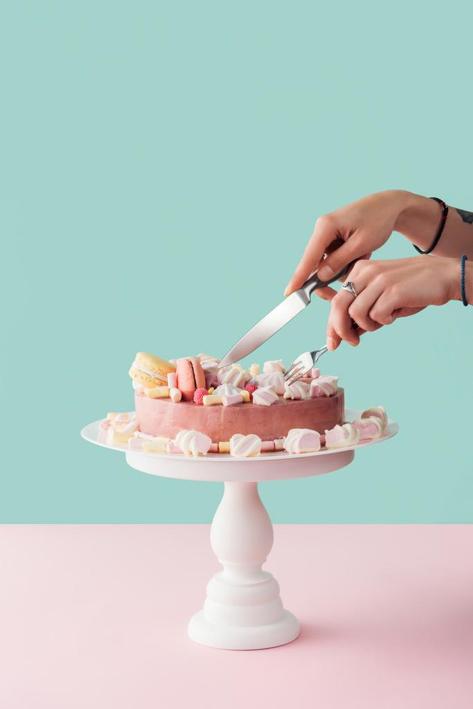 cropped view of woman cutting marshmallow cake with knife and fork on cake stand - Photo, Image