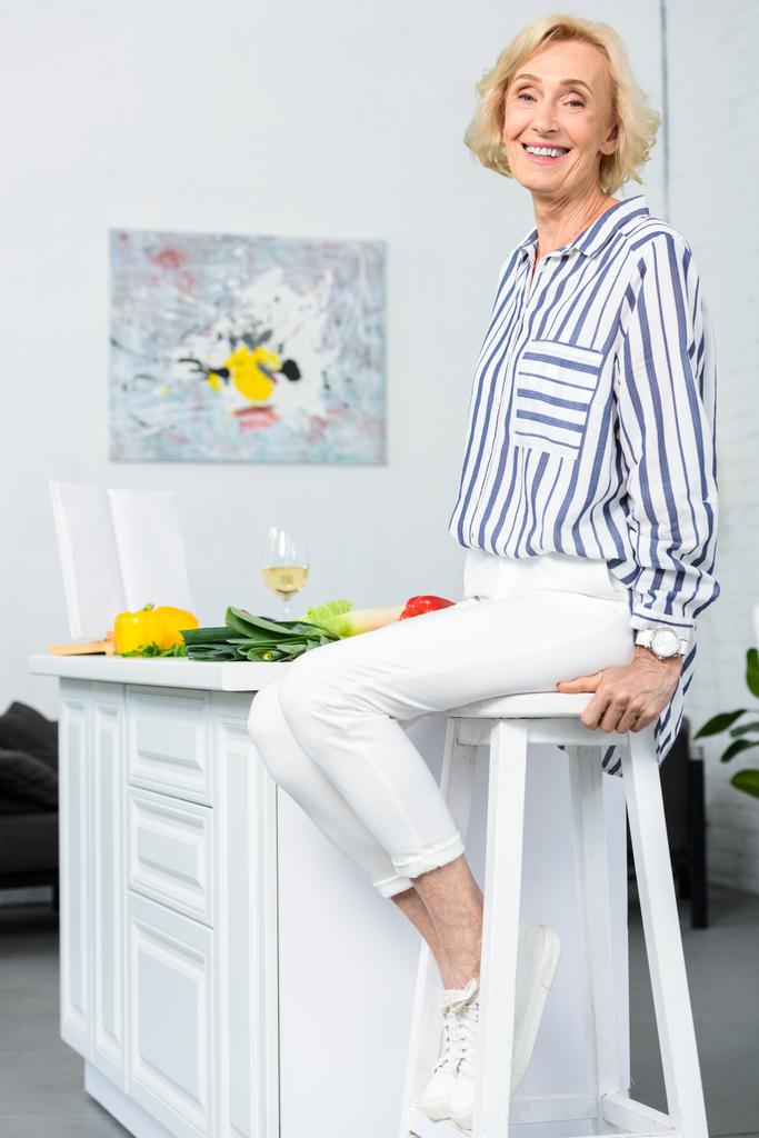 szczęśliwy atrakcyjne siwe włosy kobieta siedzi na krzesełko w kuchni  - Zdjęcie, obraz