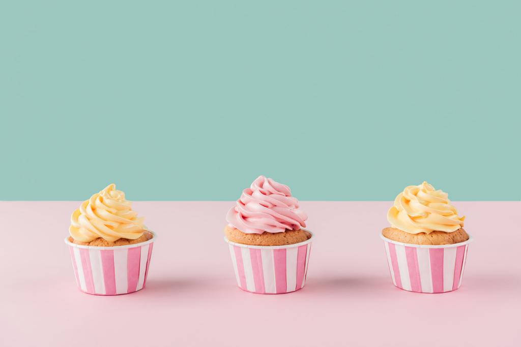 tres cupcakes con crema de mantequilla en fila sobre fondo pastel
 - Foto, imagen
