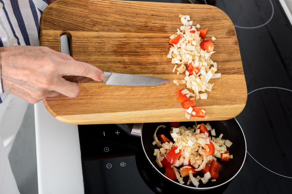 bijgesneden afbeelding van senior vrouw zetten groenten op koekenpan in keuken - Foto, afbeelding