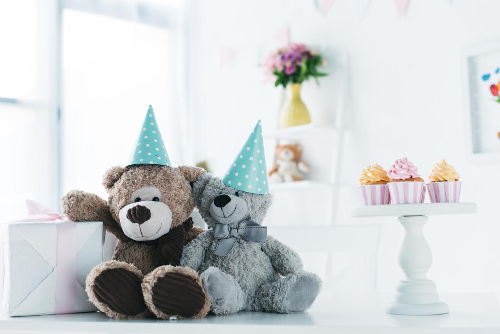 teddy bears in cones on table with gift box and cupcakes  - Photo, Image