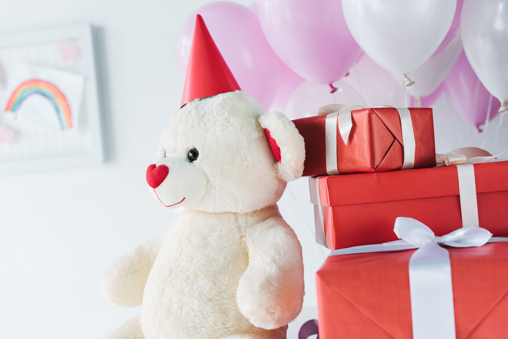 селективный фокус плюшевого мишки в конусе с подарочными коробками и воздушными шарами
  - Фото, изображение