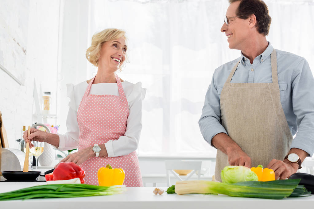 gelukkige senior paar samen koken in de keuken en kijken naar elkaar - Foto, afbeelding
