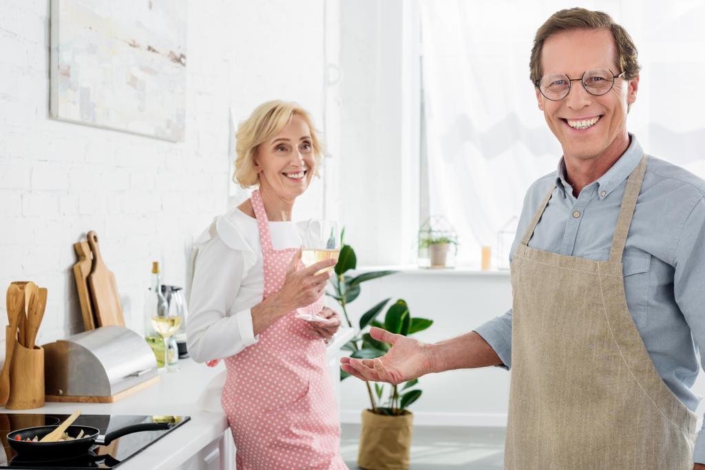 felice vecchio in grembiule e occhiali sorridente alla macchina fotografica mentre la moglie beve vino in cucina
 - Foto, immagini