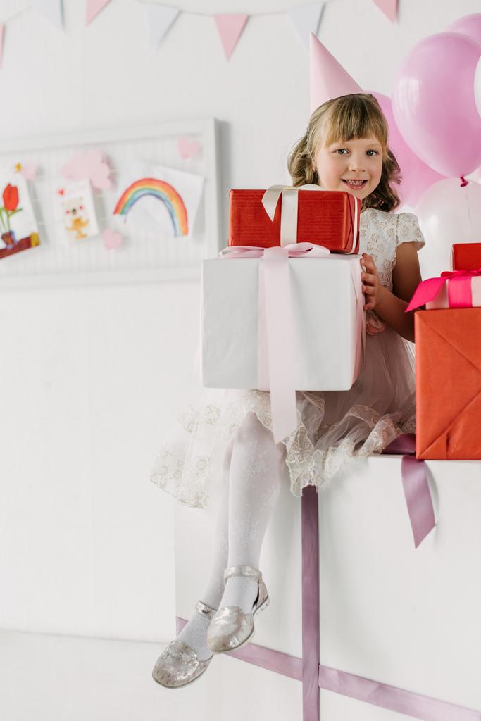 lächelndes Geburtstagskind in Tüte mit Geschenkschachteln und Blick in die Kamera - Foto, Bild