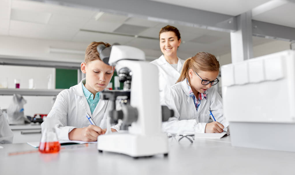 Eğitim, bilim ve çocuk kavramı - öğretmen ve öğrencilerin okul laboratuarında Kimya öğrenmek ve çalışma kitaplarına yazma - Fotoğraf, Görsel