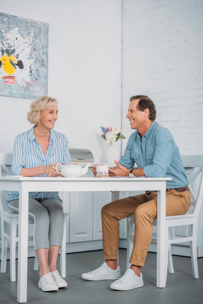 happy senior couple smiling each other while drinking tea together at home  - Photo, Image