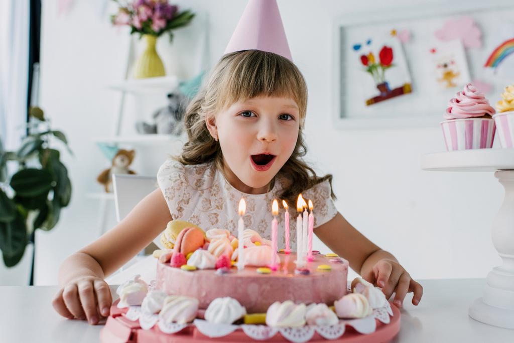 bambino sorridente nel cono che spegne le candele dalla torta di compleanno
  - Foto, immagini