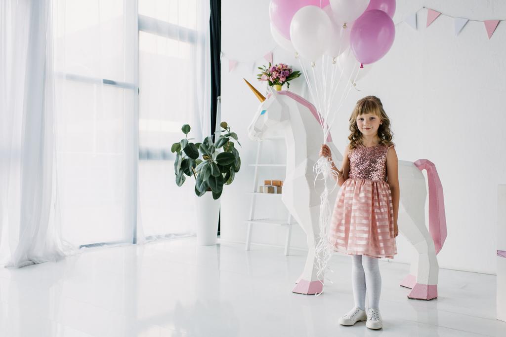 birthday kid holding bunch of air balloons and standing with decorative unicorn  - Photo, Image