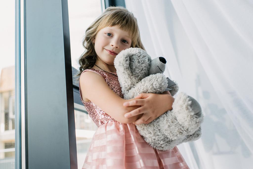 glückliches kleines Kind blickt in die Kamera und umarmt Teddybär  - Foto, Bild